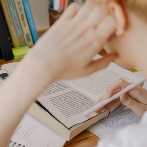 Vrouwelijke student leest in een handboek en noteert in haar notities. Dit is de omslagfoto van de pagina waarop je informatie en tips over een strategische aanpak voor een openboekexamen kan vinden. 